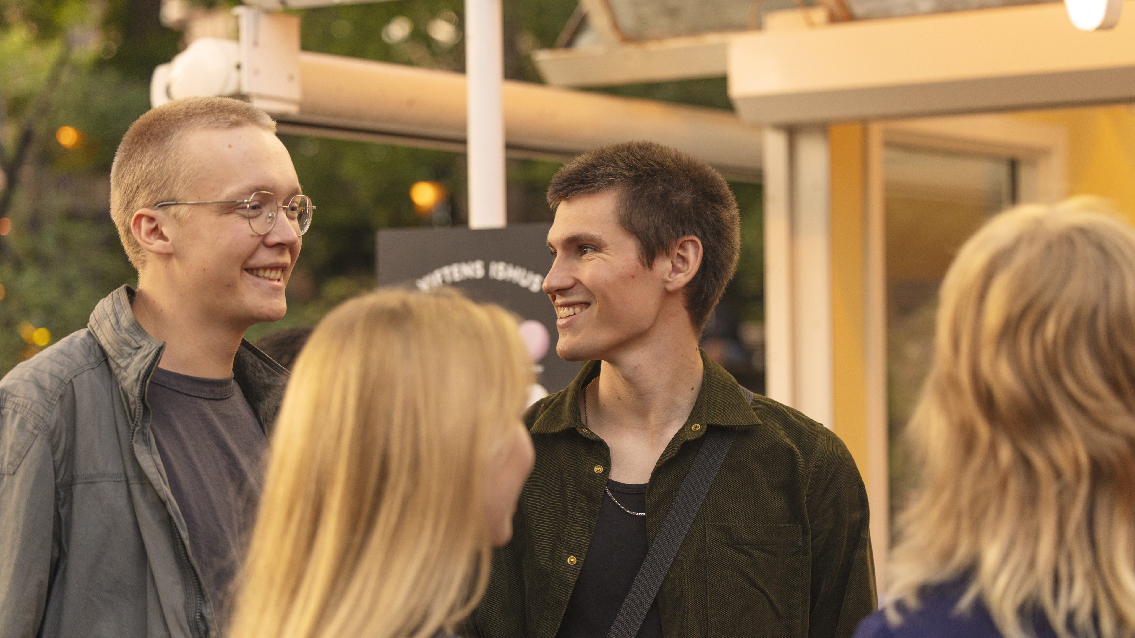 Gruppe af unge smilende personer i afslappet samtale i Tivoli i aftenslys.