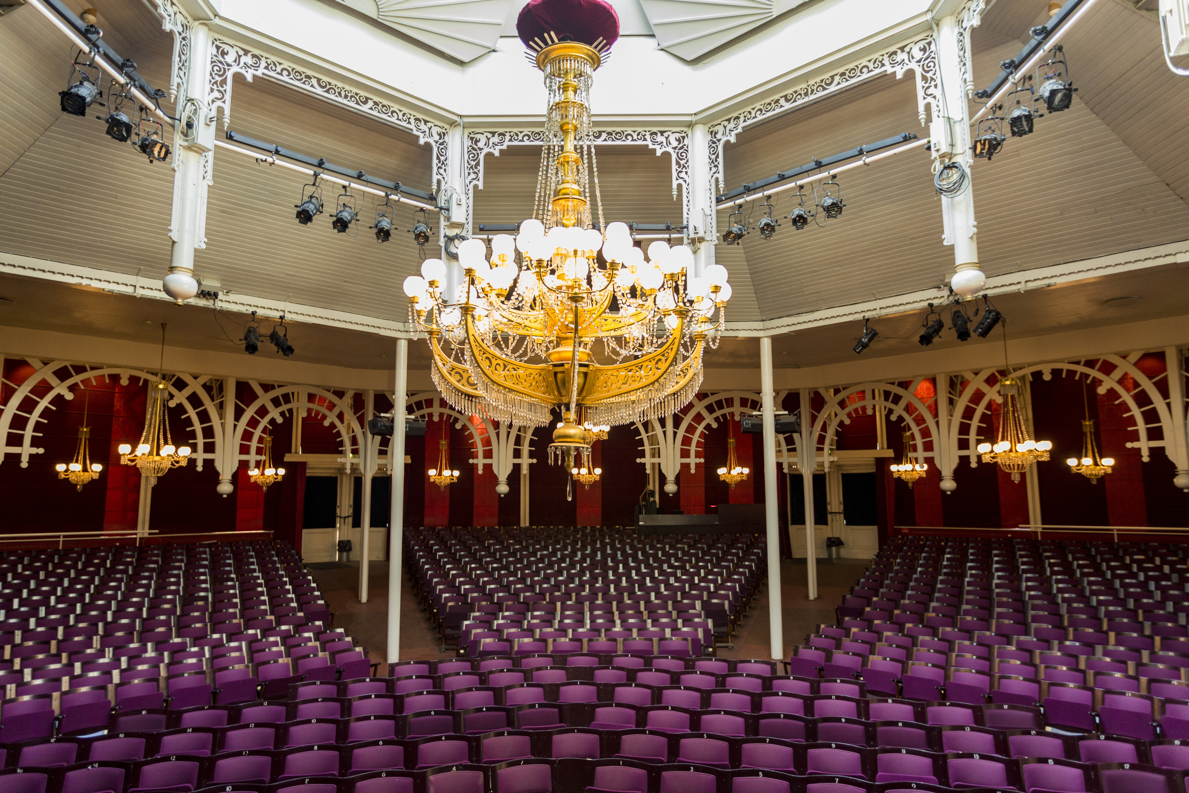  The Glass Hall Theatre in Tivoli, illuminated by a large golden chandelier and surrounded by rows of purple seats, available for rent by external organizers for shows and performances.