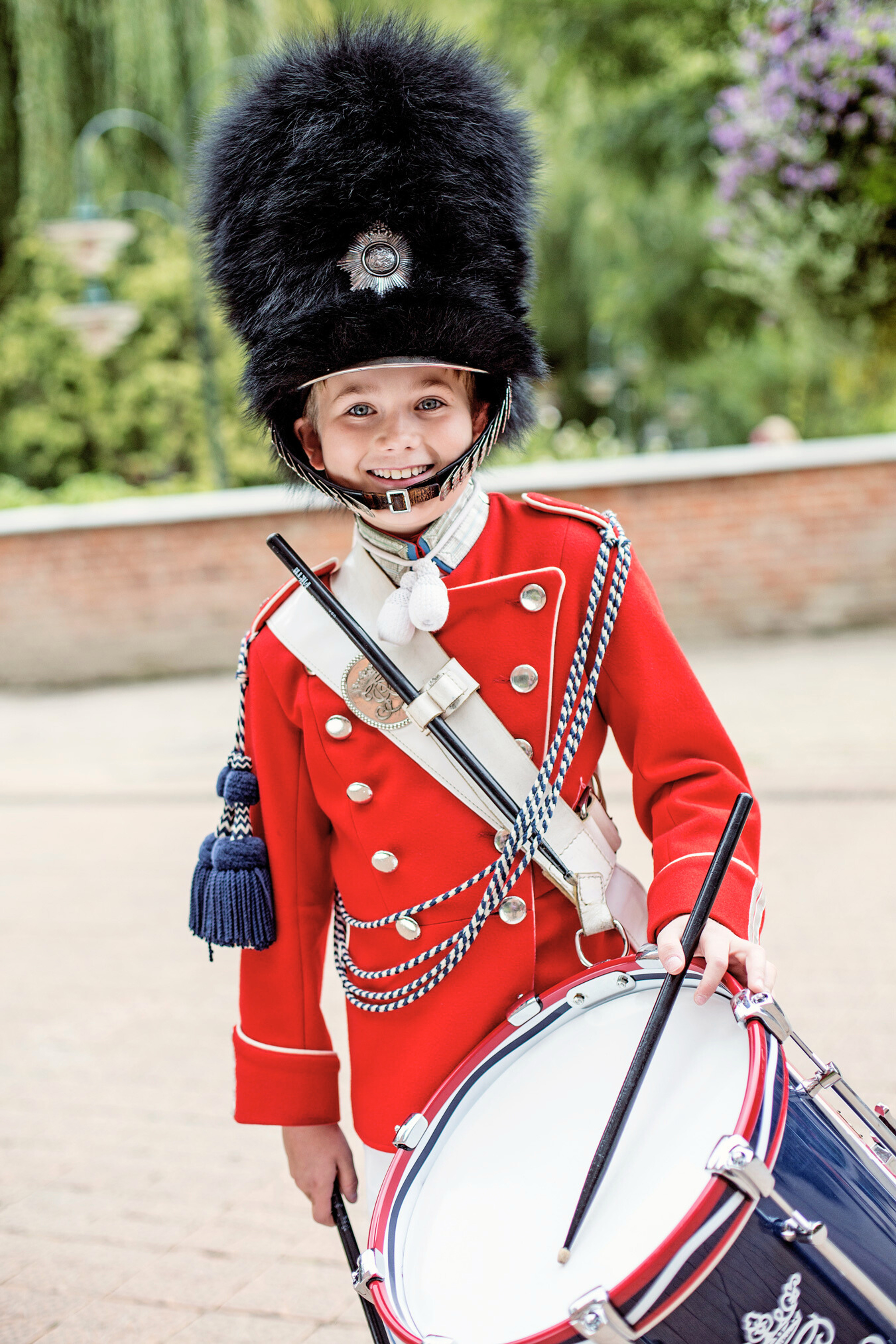 En ung trommeslager fra Tivoli-Garden iført den klassiske røde uniform og sorte bjørneskindshue. Han holder trommestikker og står med en tromme.