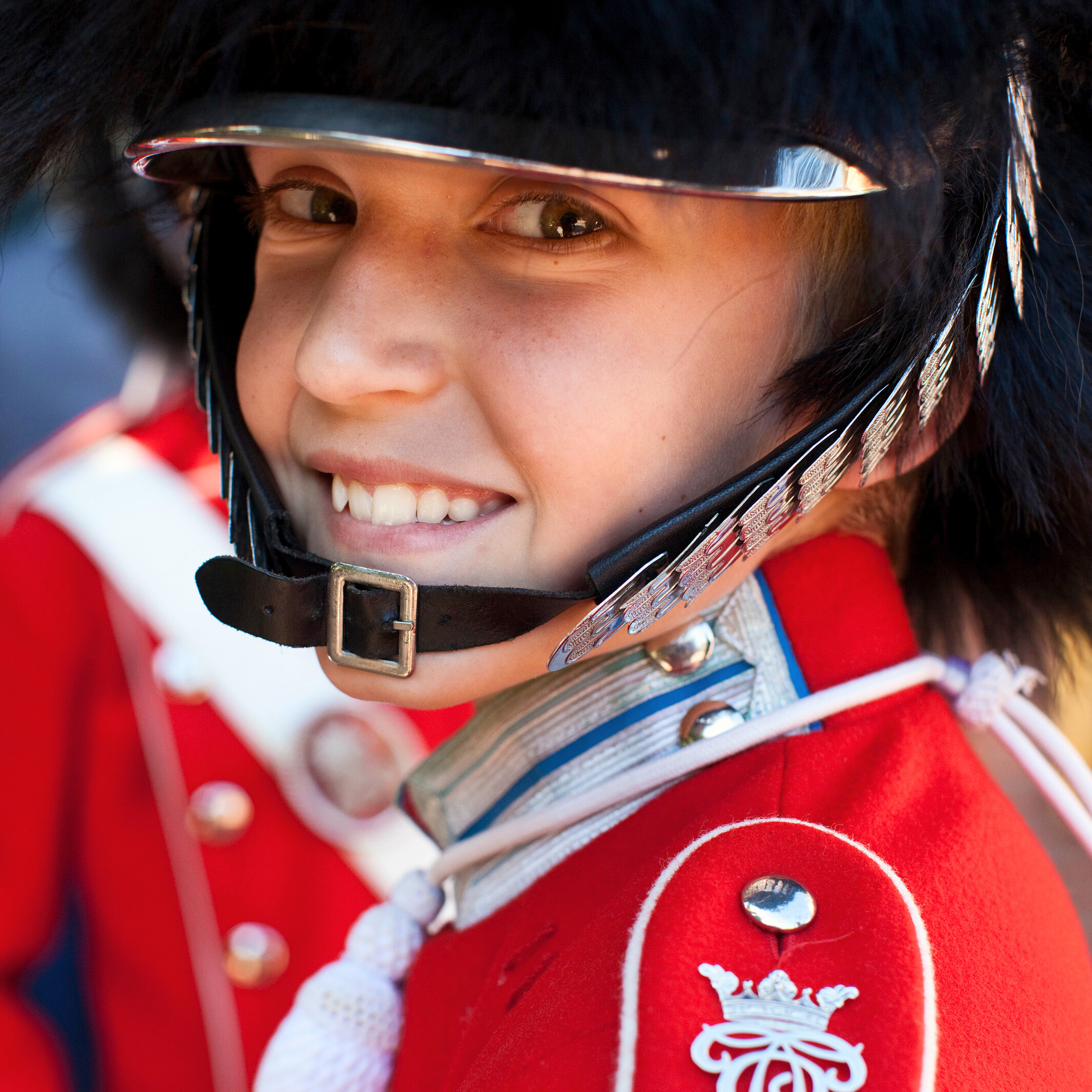  A smiling Tivoli guard wearing a red uniform and a black helmet. The guard is looking directly at the camera, appearing happy.