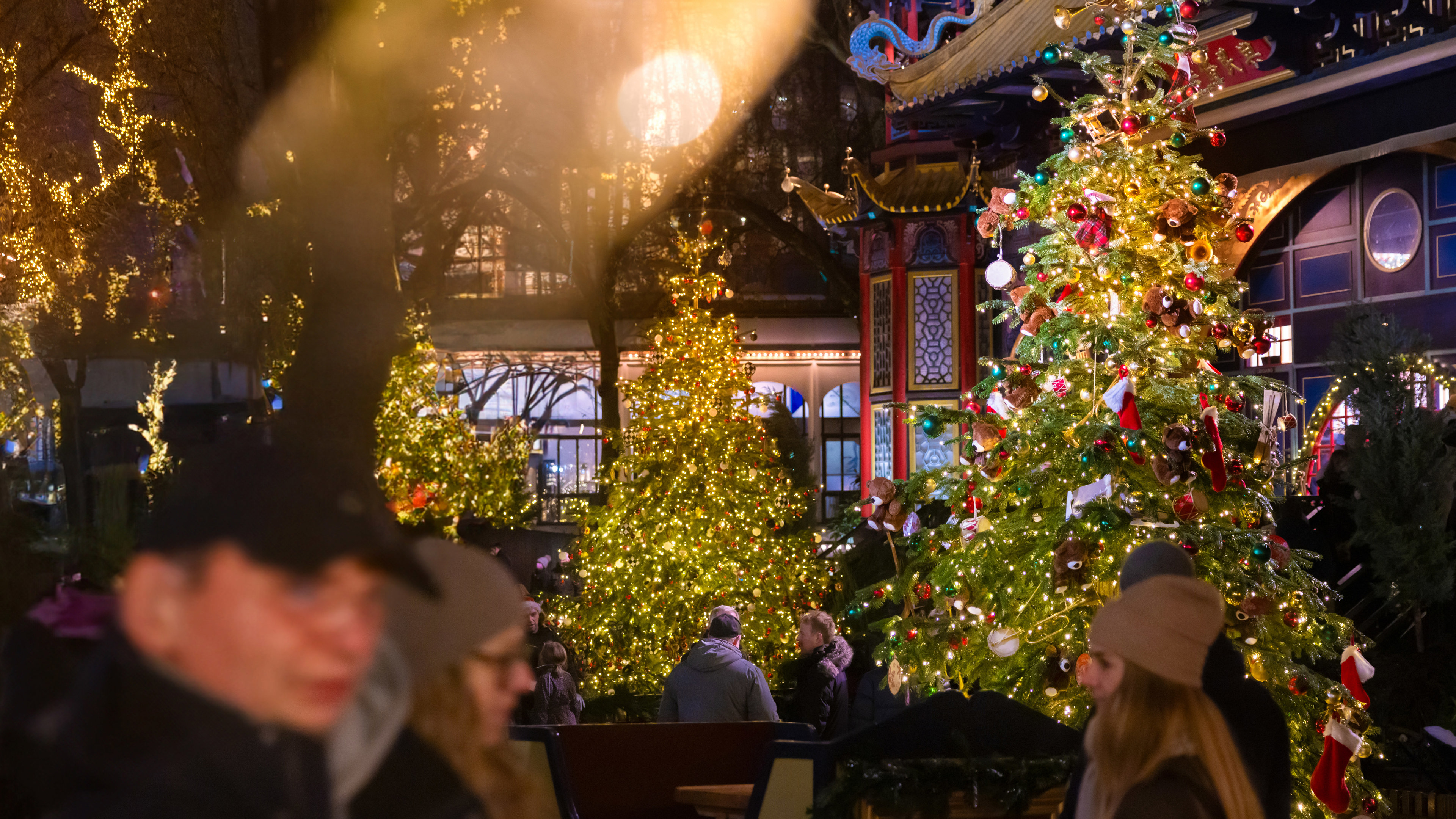 Tivoli er pyntet op til jul med farverige juletræer og lys, som skaber en hyggelig og festlig stemning.