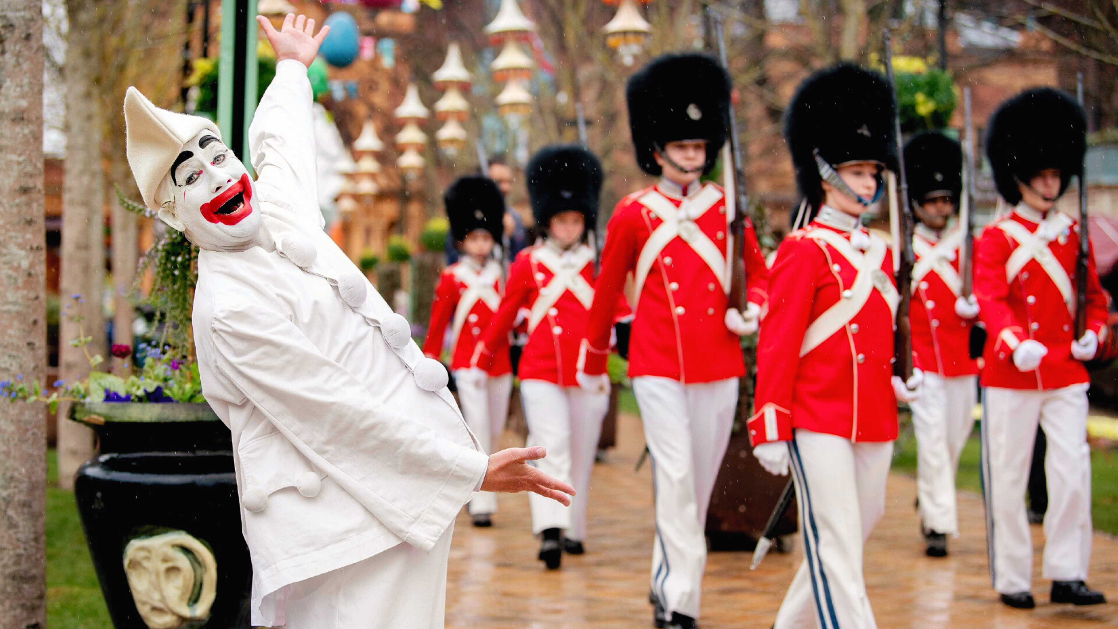 Pierrot danser foran Tivoli-Garden under en parade. Gardere i røde uniformer og hvide bukser marcherer bag ham i takt.