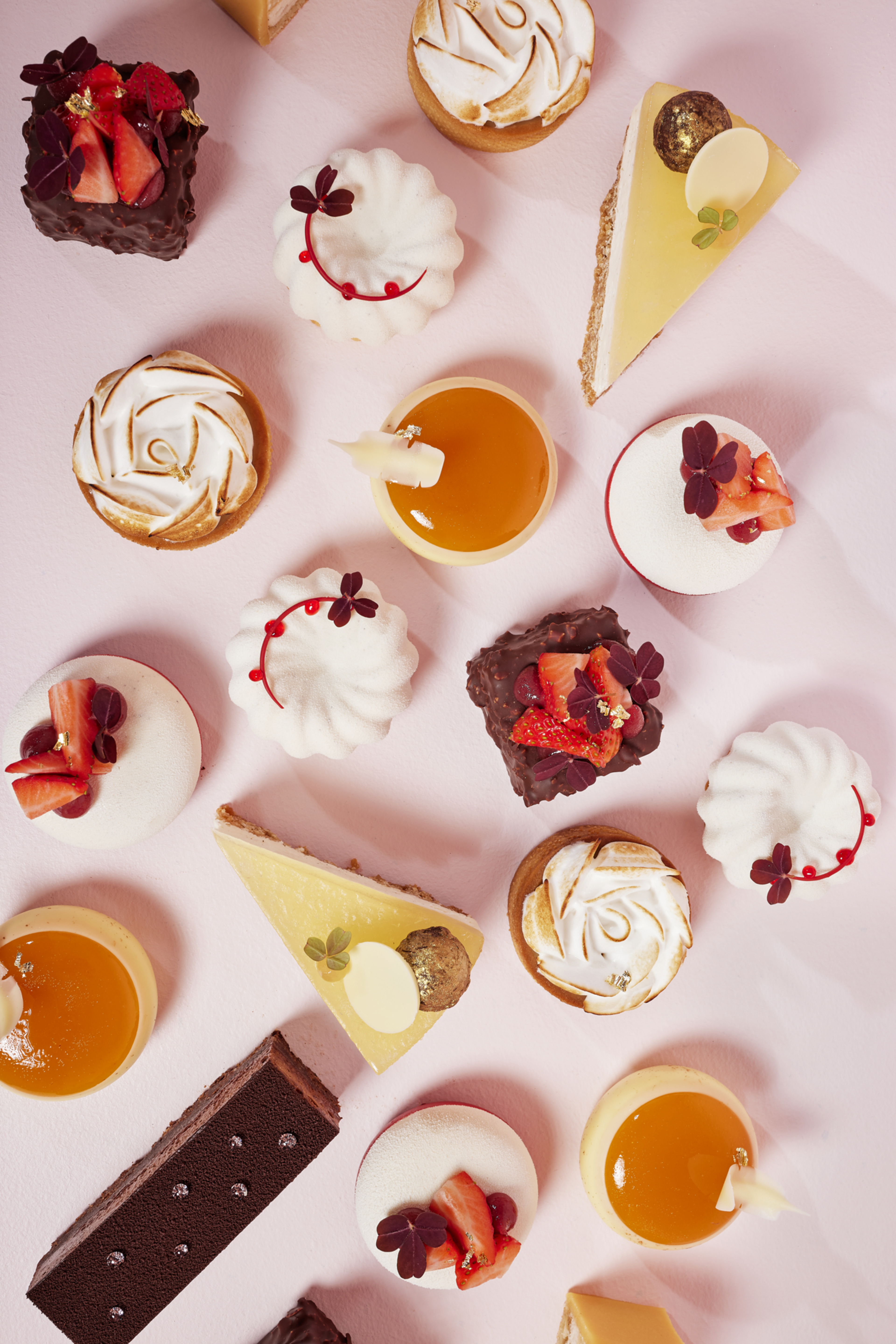 An assortment of colorful desserts and pastries, including mini cakes and chocolate, on a pink background.