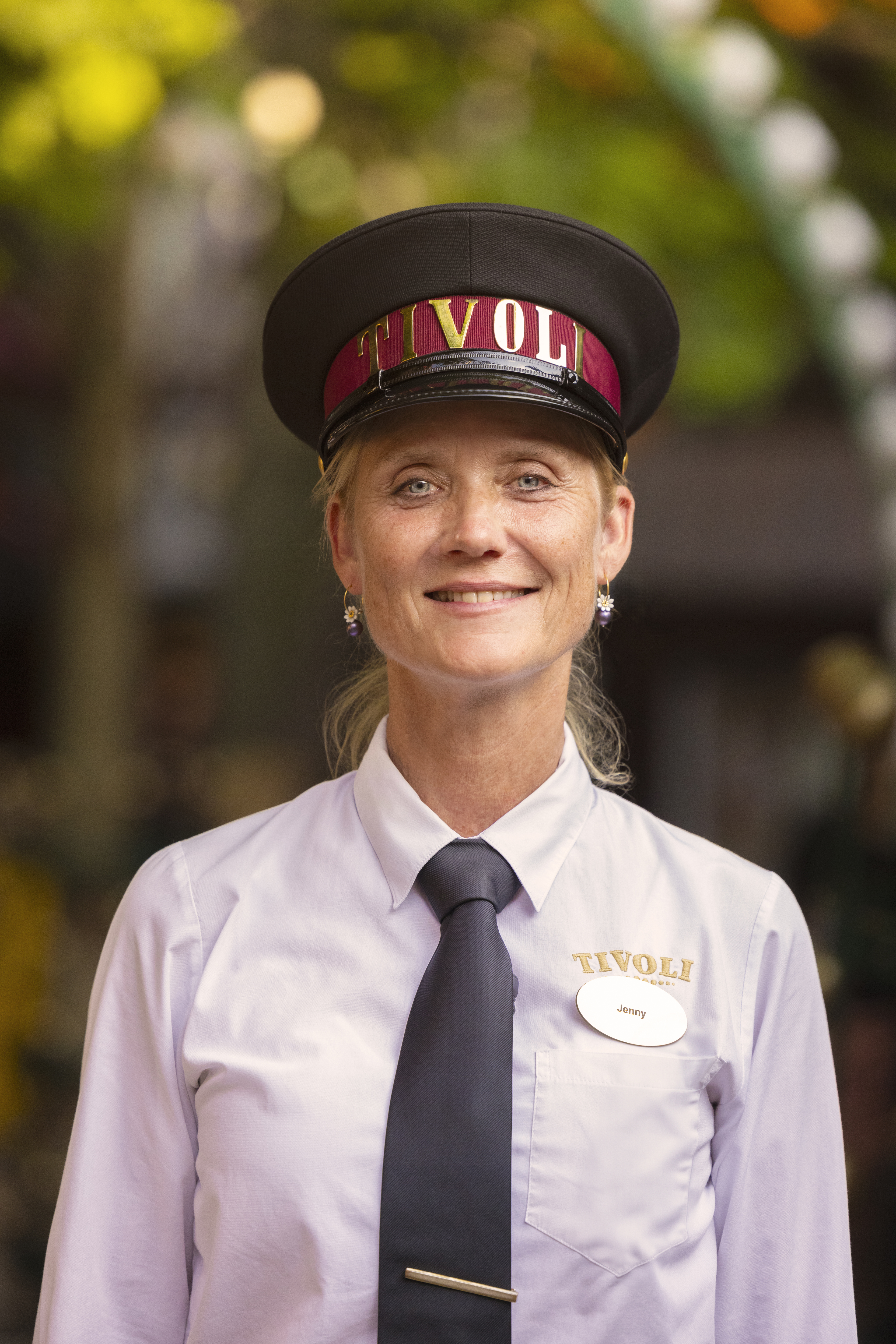 Kvindelig medarbejder iført Tivoli-uniform og kasket smiler til kameraet.